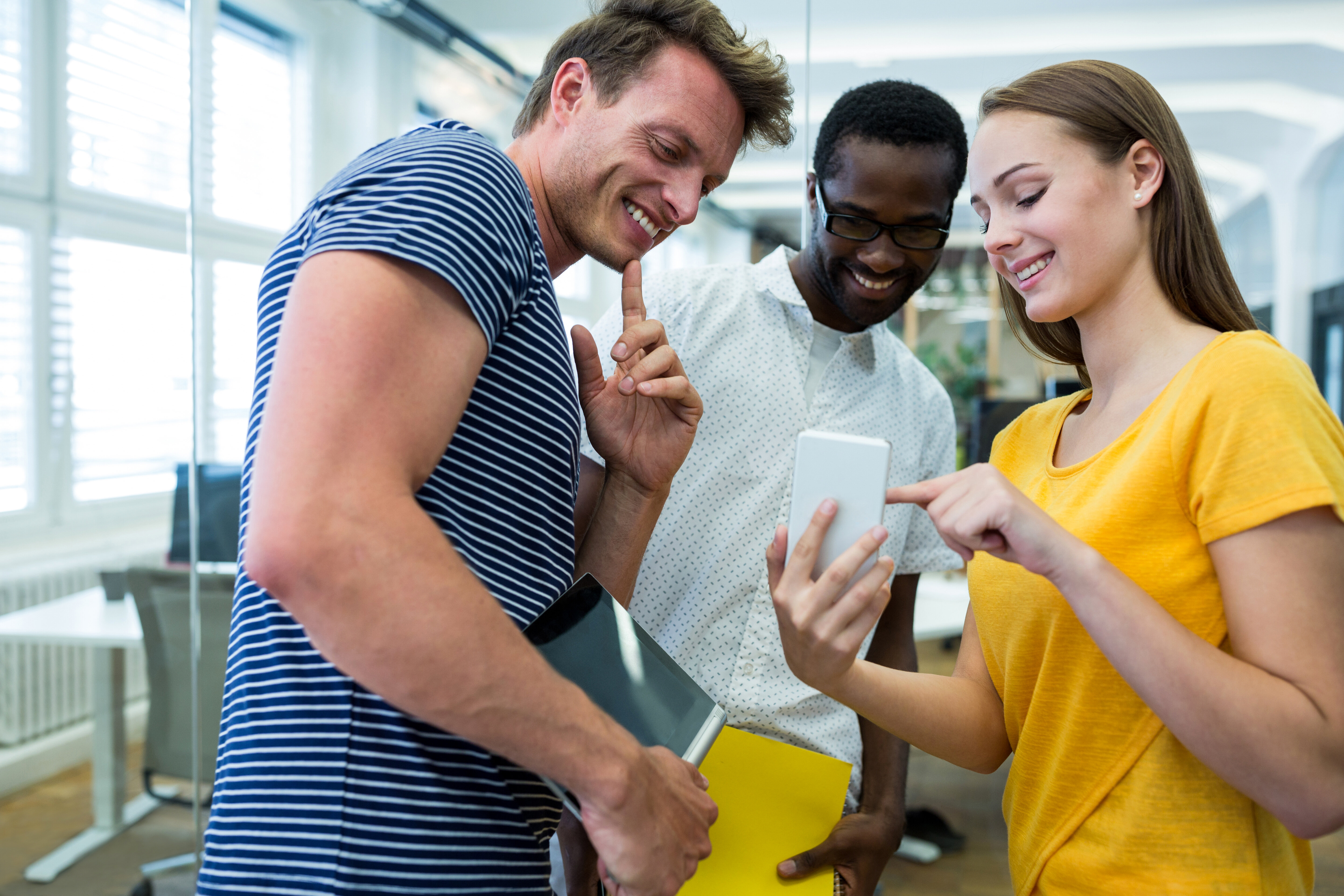Three employees collaboratively examining a cell phone, engaged in discussion and sharing insights