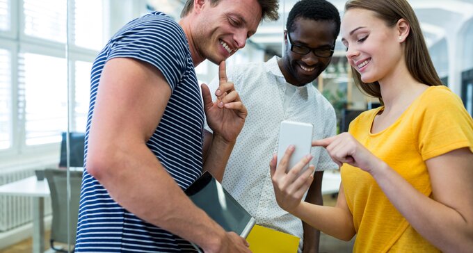 Three employees collaboratively examining a cell phone, engaged in discussion and sharing insights