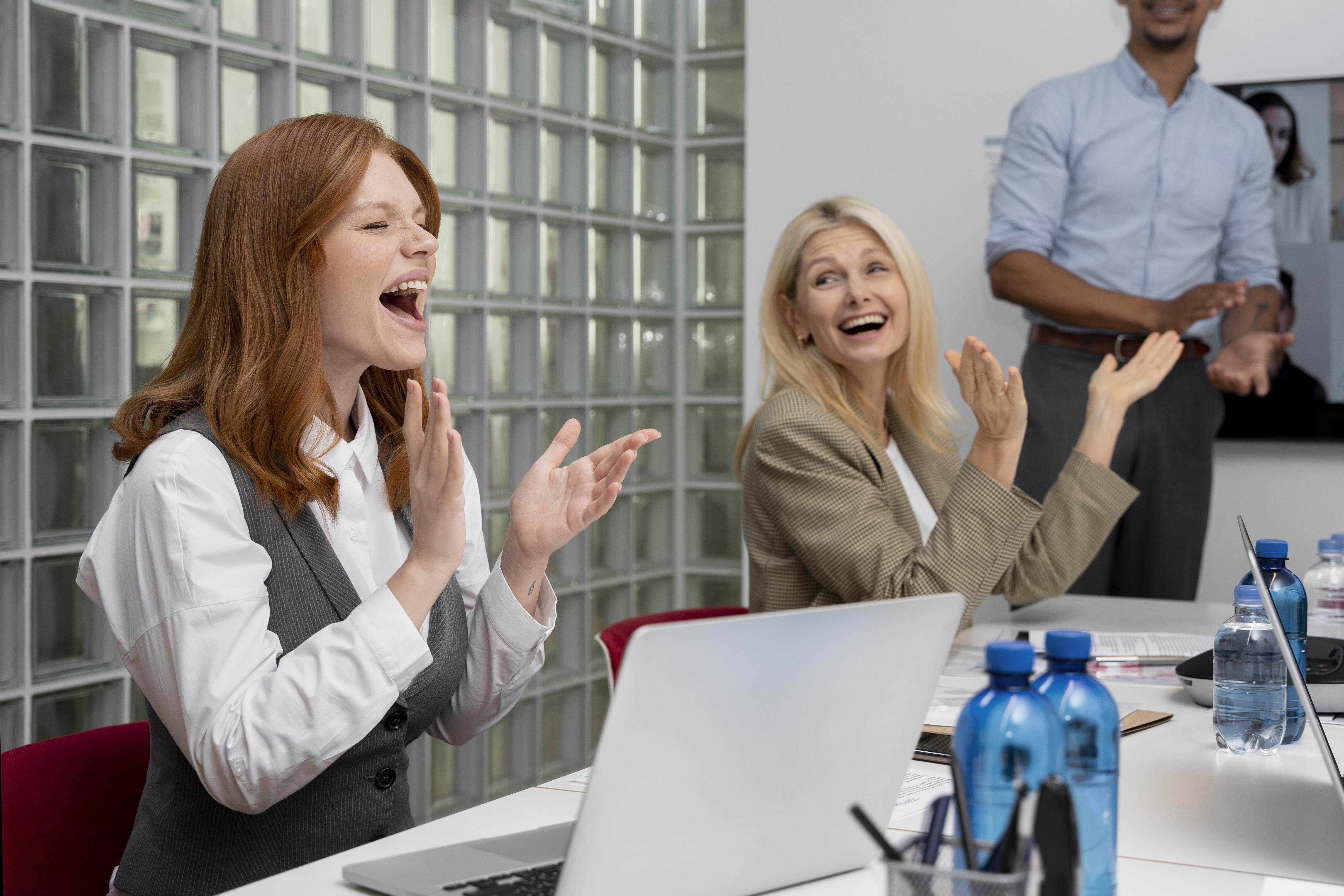 Drei Mitarbeiter applaudieren während eines Meetings in einem modernen Büro