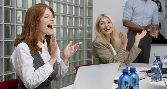 Three employees applaud during a meeting in a modern office