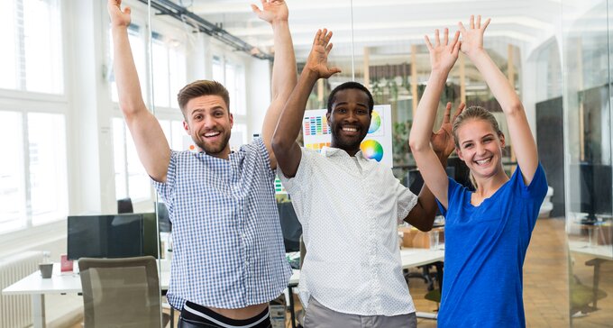 A group of UX designers in an office, celebrating and throwing their hands up in the air