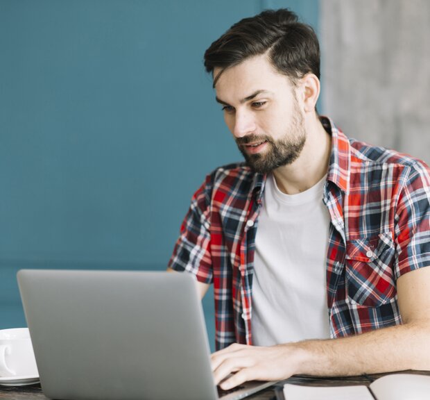 IT-Systemadministrator, sitzt an einem Tisch und arbeitet an seinem Laptop