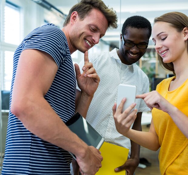 Three employees gathered around a cell phone, looking at content