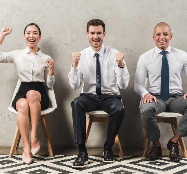 Three employees express joy after successful hiring, seated on chairs with arms lifted
